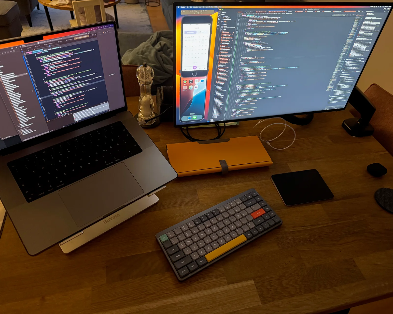 A warm developer desk with a laptop, external monitor, code and a compact keyboard